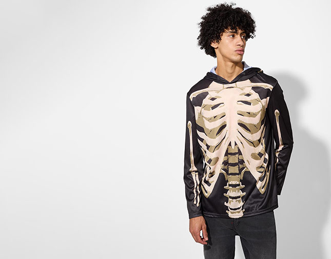 Man wearing a black hoodie with a skeleton print and dark jeans against a light background.