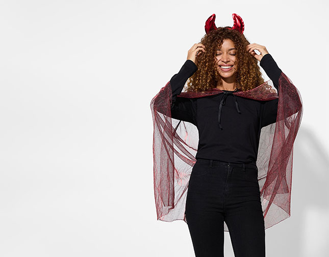 Smiling woman wearing red devil horns and a sheer red spiderweb cape over a black outfit.